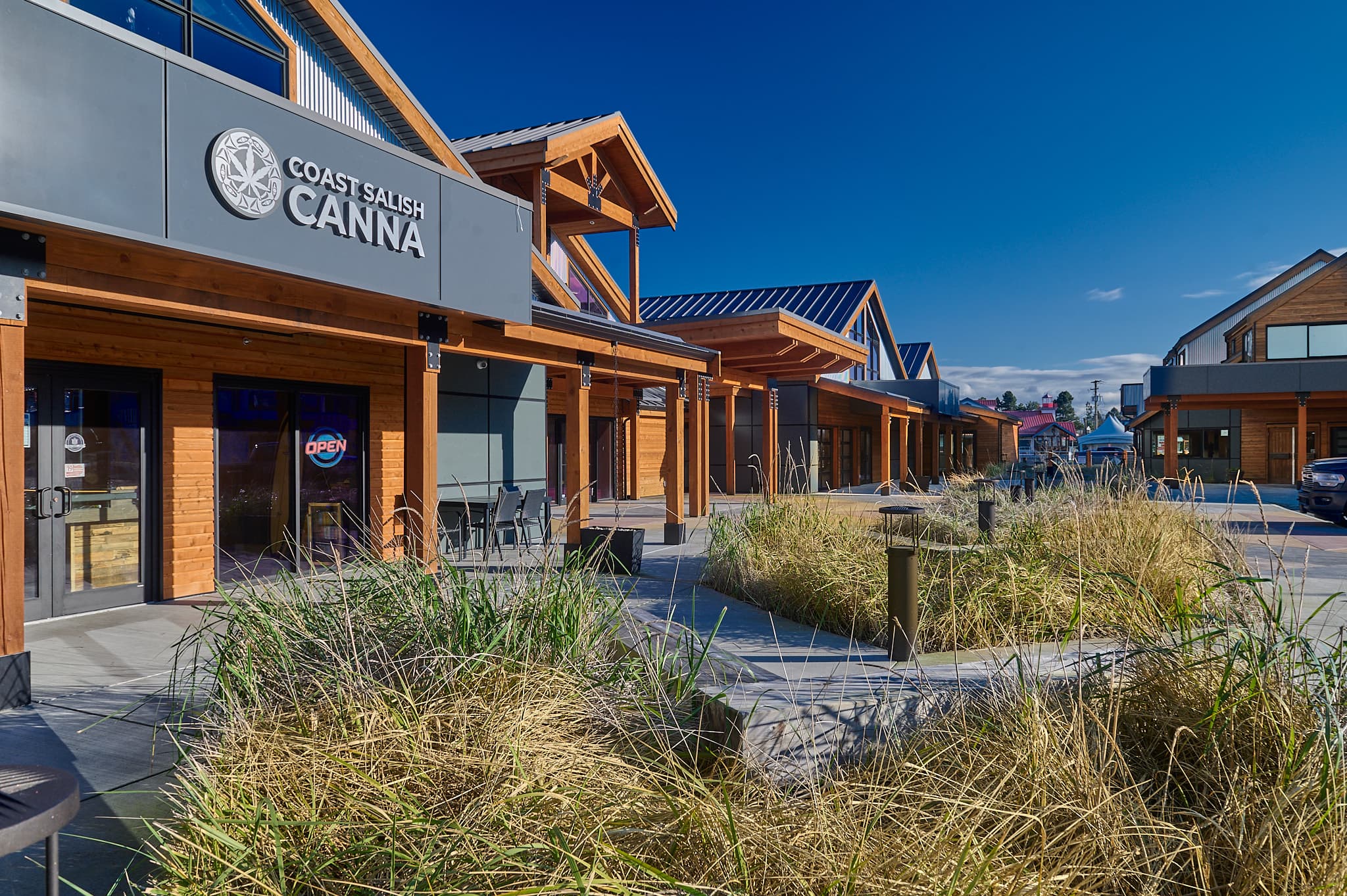Modern wood-paneled Coast Salish Canna storefront with tall grasses and a clear blue sky.