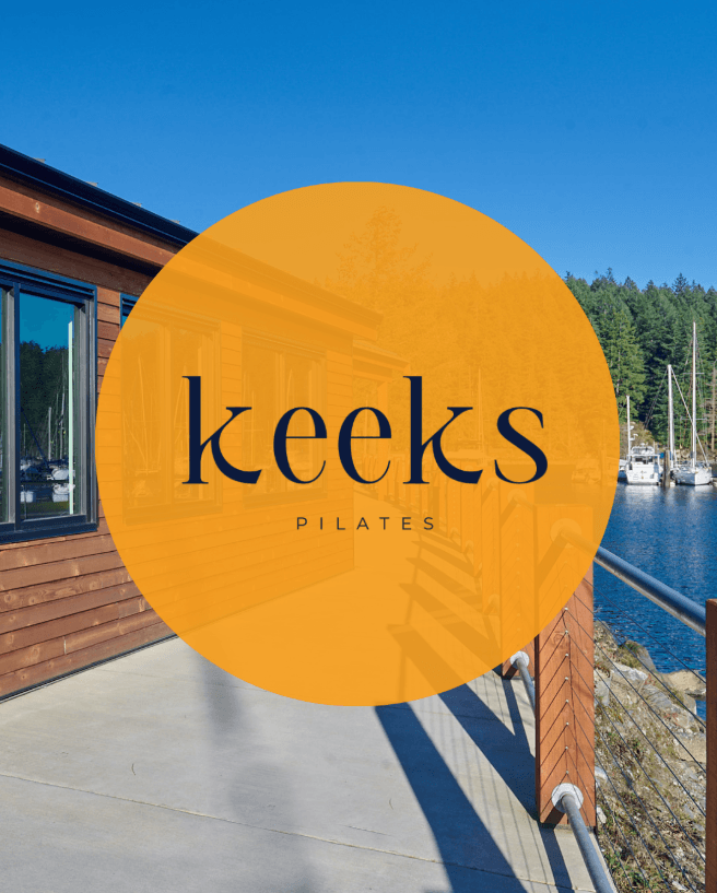 Wooden building overlooking a marina with a large orange circle logo for Keeks Pilates.