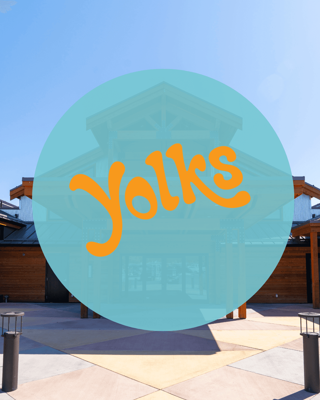 Orange stylized 'Yolks' in a blue circle over a wooden building and geometric courtyard.